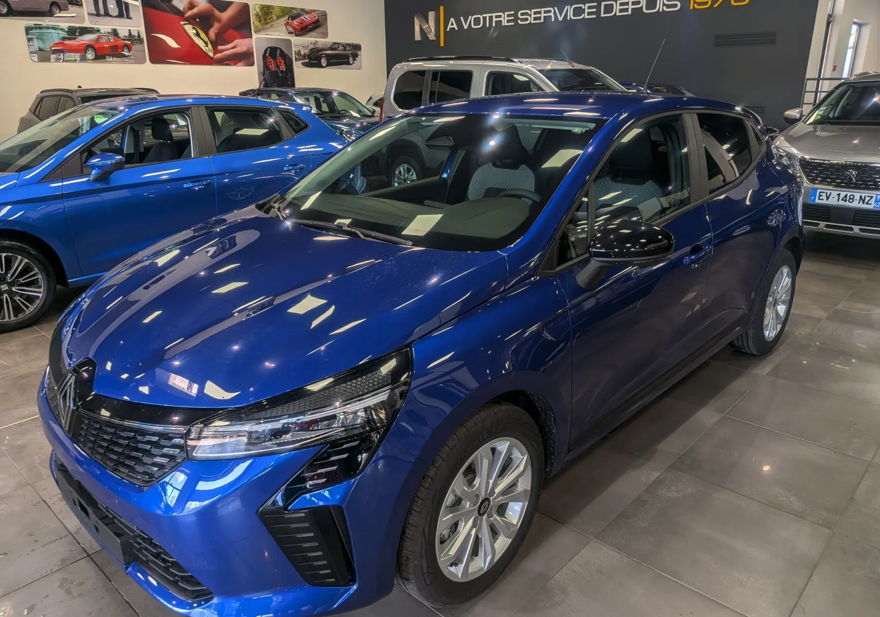 Renault Clio V Bleu Iron vue 3/4 avant droit en intérieur, avec jantes alliage et calandre noire brillante.