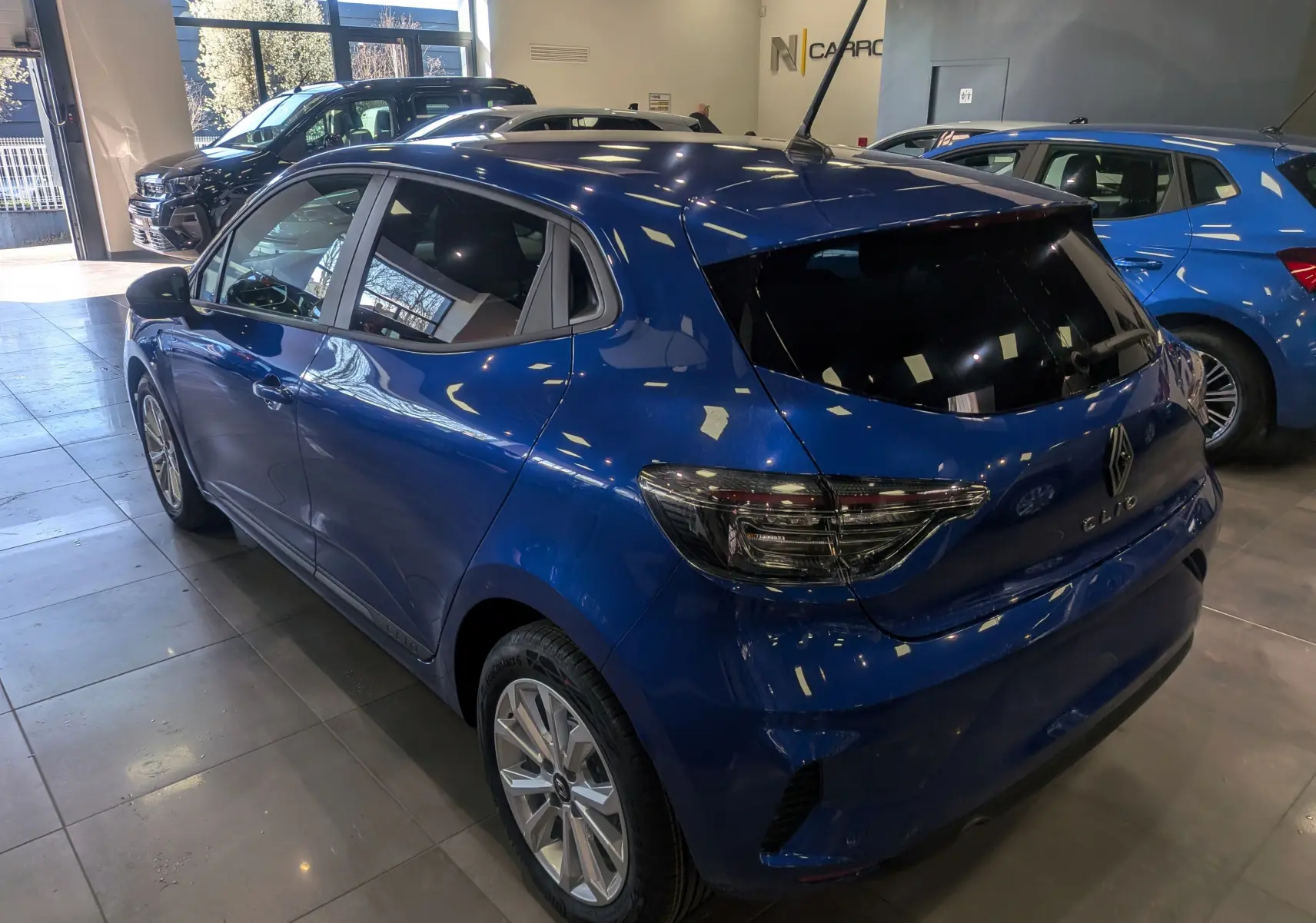 Vue 3/4 arrière droite d'une Renault Clio V Bleu Iron avec vitres teintées et jantes alliage en showroom.