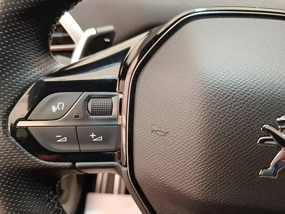 Gros plan sur les commandes gauche du volant cuir du Peugeot 3008 hybride bleu, avec logo lion visible.