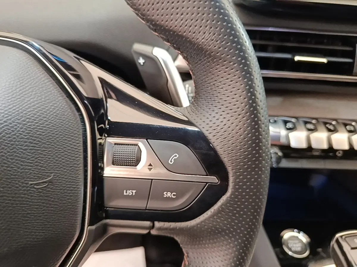 Gros plan sur le volant cuir perforé côté gauche du Peugeot 3008 bleu avec commandes audio et téléphone intégrées.