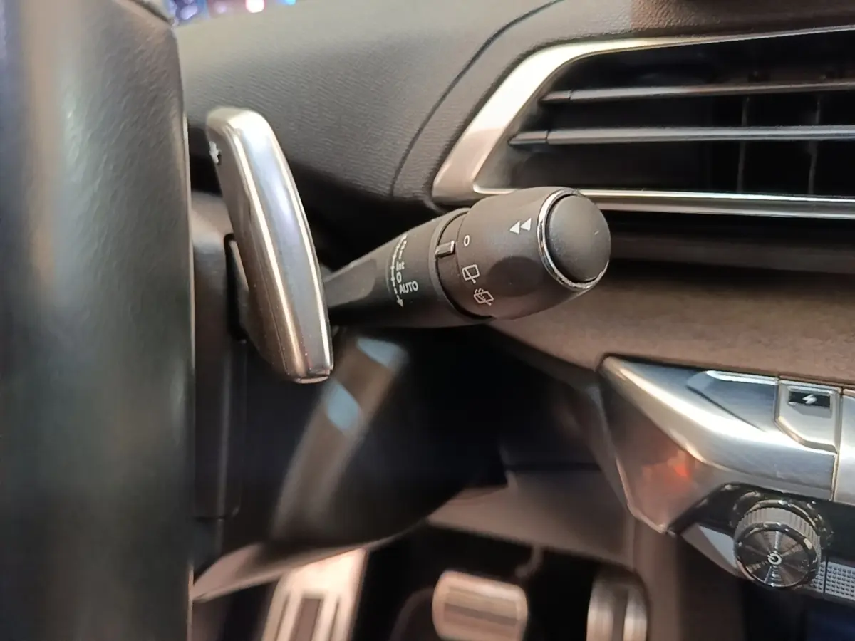 Gros plan sur la manette de commande des essuie-glaces côté gauche du tableau de bord noir du Peugeot 3008 bleu hybride.