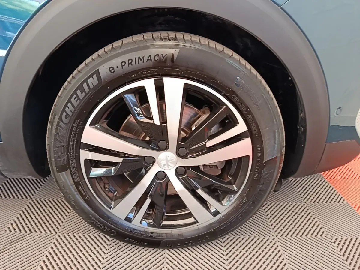 Gros plan sur la roue avant droite du Peugeot 3008 bleu, jante alliage bicolore et pneu Michelin e-Primacy.