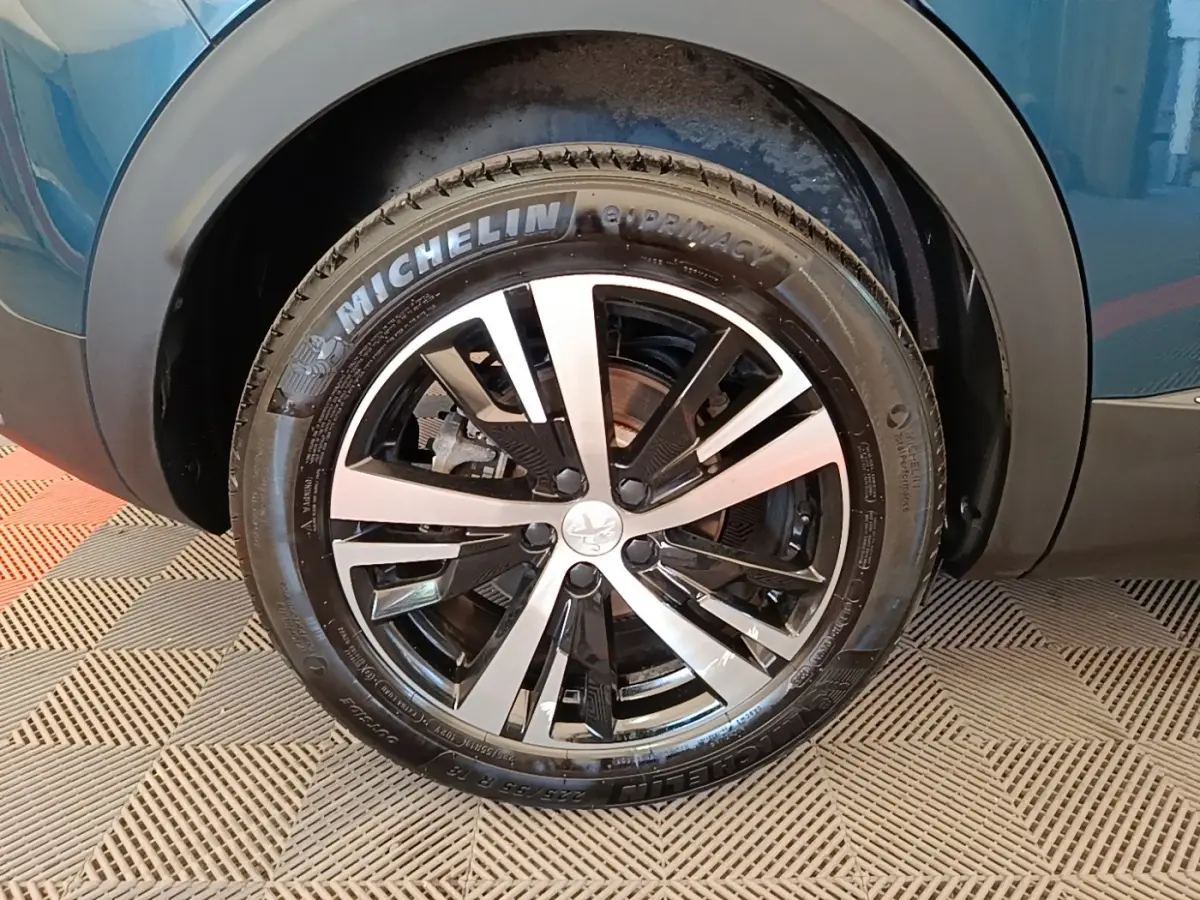 Gros plan sur la roue avant droite du Peugeot 3008 bleu, avec jante alliage bicolore et pneu Michelin.