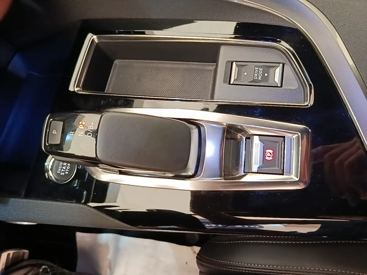 Gros plan sur la console centrale noire brillante du Peugeot 3008 Hybrid 225, avec levier de vitesse et bouton de frein à main électrique.