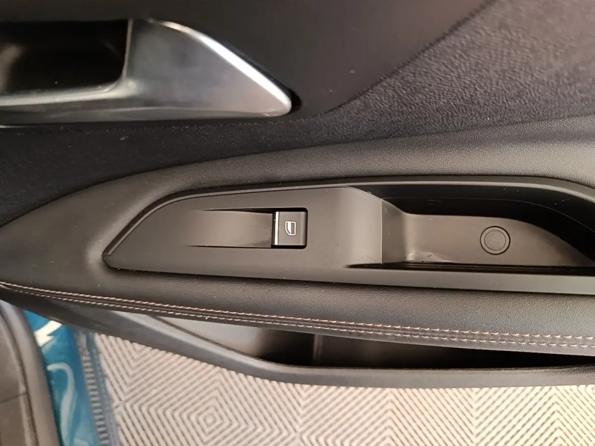 Gros plan sur la commande de lève-vitre côté gauche en plastique noir avec surpiqûres marron, intérieur Peugeot 3008 bleu visible.
