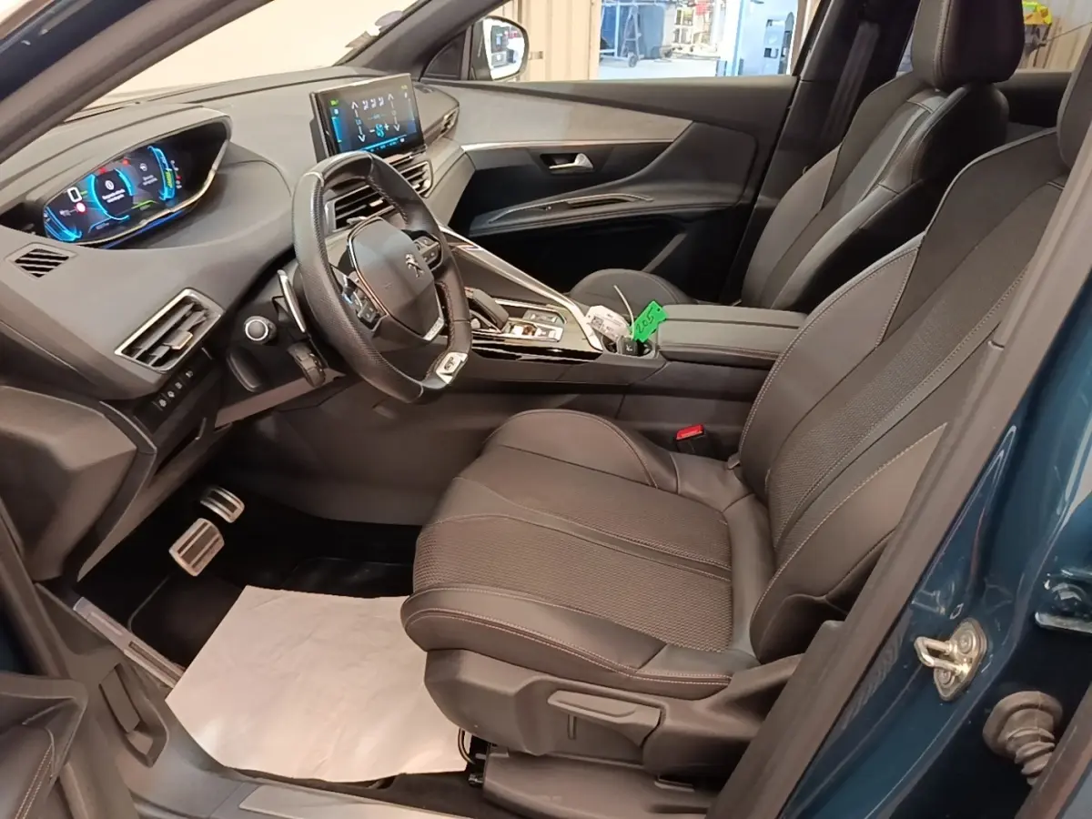 Vue intérieure côté conducteur du Peugeot 3008 hybride bleu 2022, avec tableau de bord digital et sièges en tissu noir.