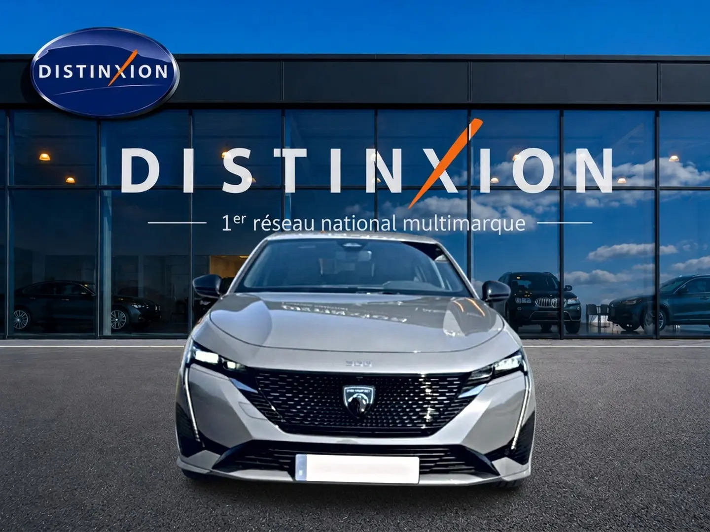 Vue avant d'une Peugeot 308 gris métallisé 2025 avec calandre noire et phares LED fins, devant une vitrine Distinxion.