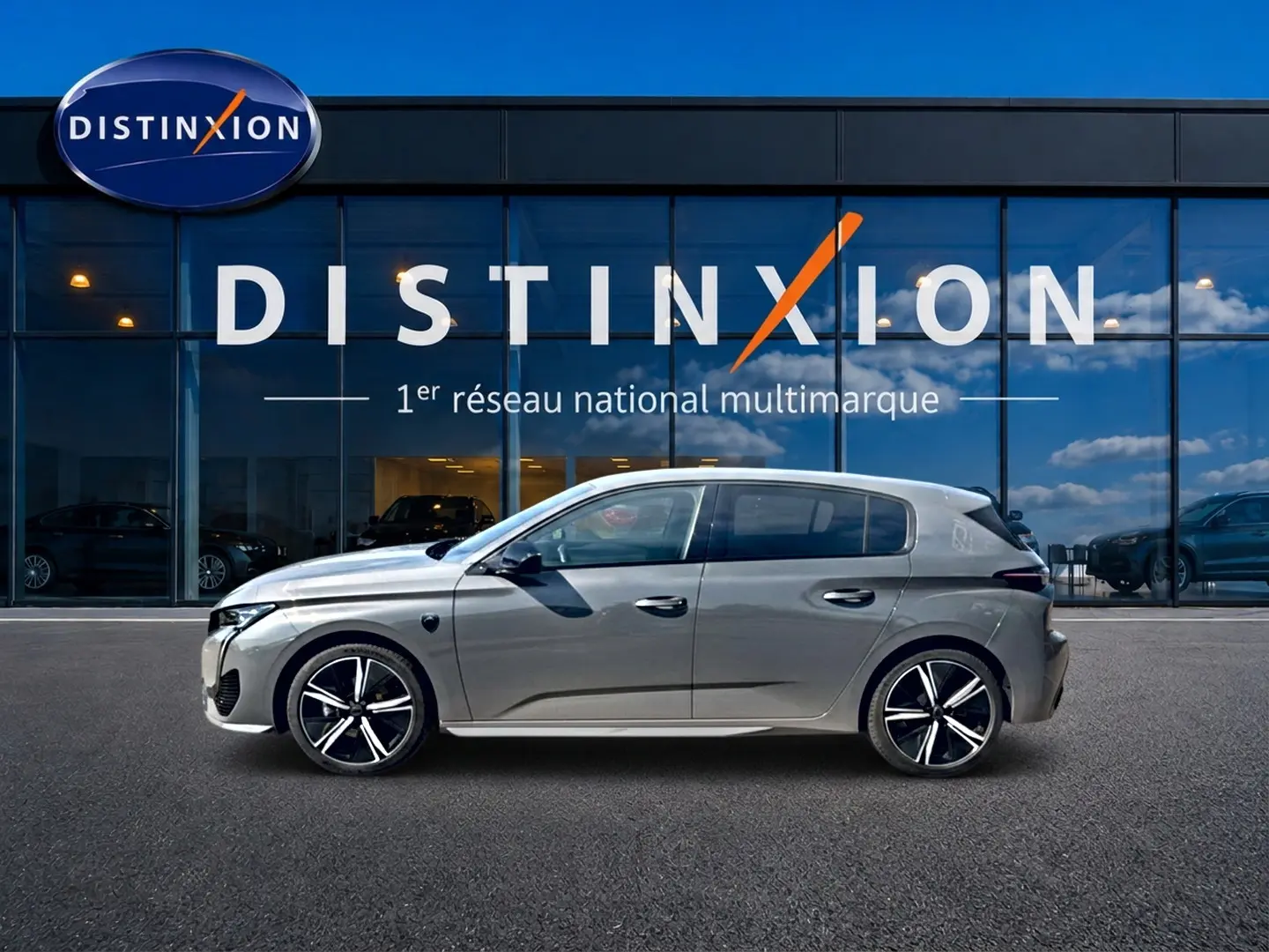 Profil droit d’une Peugeot 308 gris métallisé 2025 avec jantes alliage noires devant un showroom Distinxion.