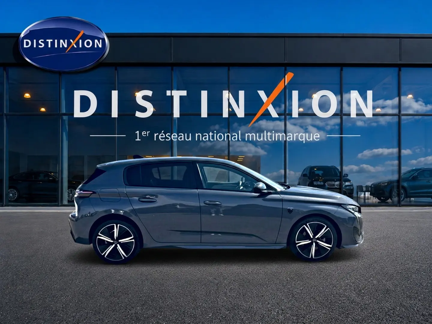 Profil côté gauche d'une Peugeot 308 gris métallisé 2025, avec jantes alliage et vitres teintées, devant une vitrine Distinxion.