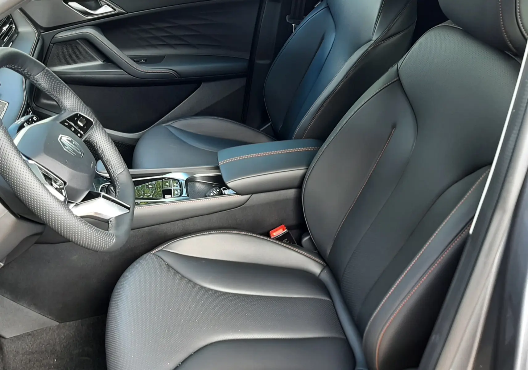 Vue intérieure côté conducteur du MG MOTOR EHS 1.5 HYBRID+ 224CH Luxury 2026, sièges cuir noir avec surpiqûres contrastées.
