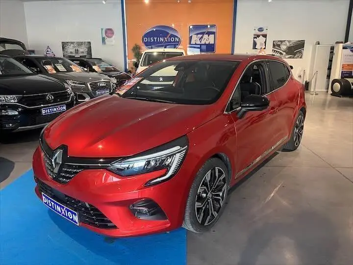 Renault Clio V rouge flamme métal vue 3/4 avant droit en showroom avec jantes alliage noires et phares LED.