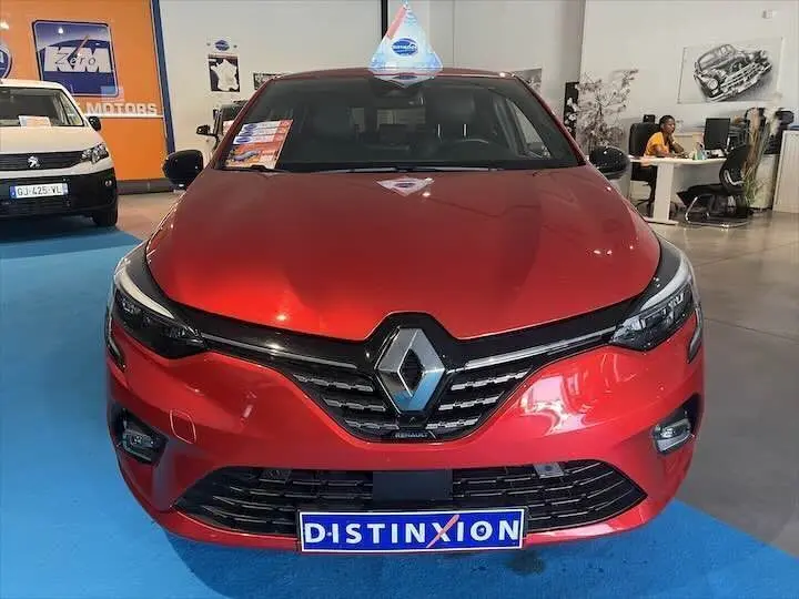 Renault Clio V rouge flamme métal vue de face en intérieur, avec logo Renault et plaque Distinxion visible.