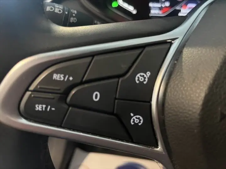 Gros plan sur les commandes de régulateur de vitesse au volant d'une Renault Clio V rouge flamme métal.