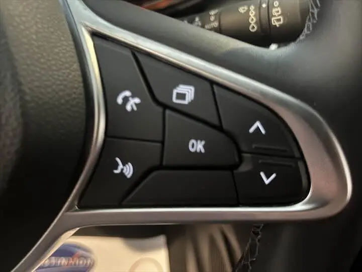 Gros plan sur les commandes au volant côté droit de la Renault Clio V rouge flamme, avec boutons multifonctions rétroéclairés.