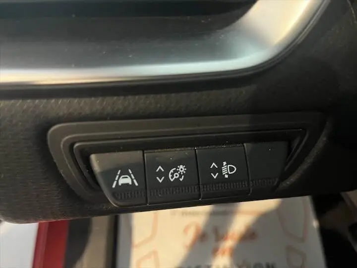 Gros plan sur les boutons de réglage des aides à la conduite dans une Renault Clio V rouge flamme métal.