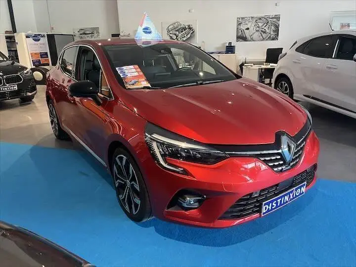 Renault Clio V rouge flamme métal vue 3/4 avant droit en showroom avec plaques Distinxion visibles