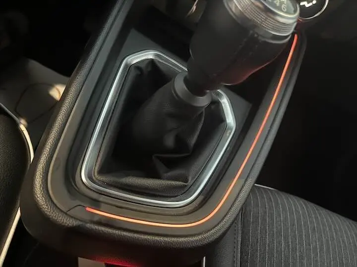 Le levier de vitesses manuel noir de la Renault Clio V rouge flamme métal, avec un éclairage d'ambiance orange autour.