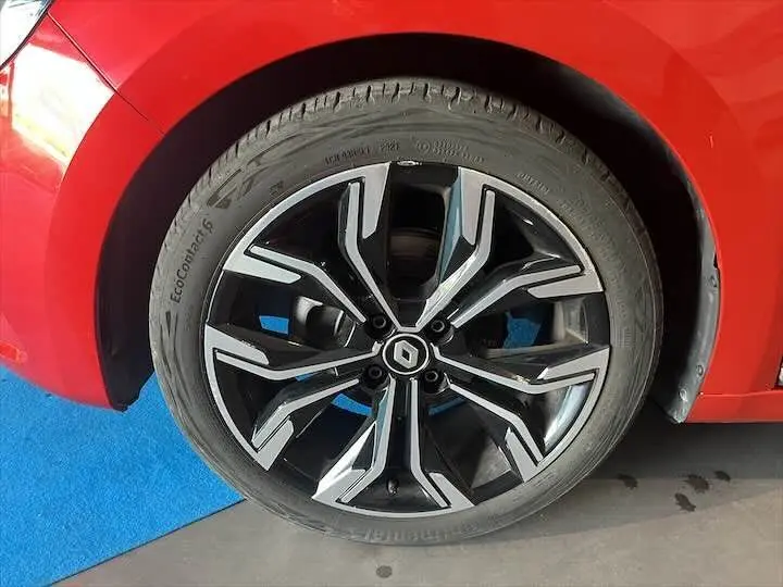 Gros plan sur la roue avant gauche d'une Renault Clio V rouge flamme métal avec jante alliage noire et argentée.