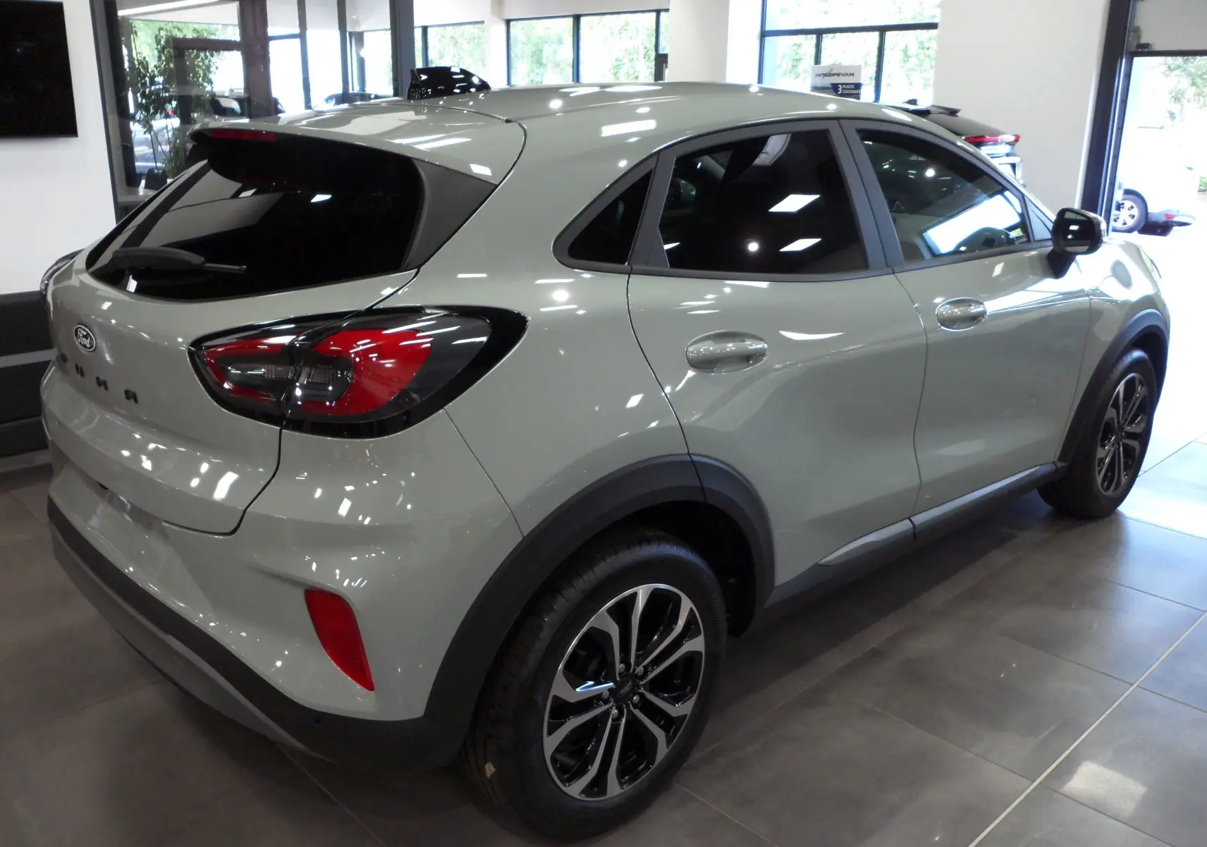 Ford Puma gris Cactus vu de trois quarts arrière droit avec jantes biton et feux arrière LED dans un showroom.