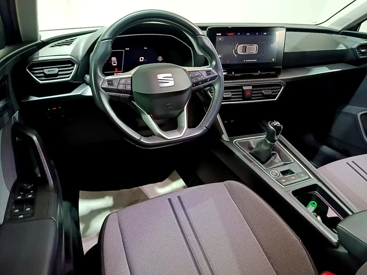 Vue intérieure du poste de conduite du SEAT Leon 2023, volant cuir multifonctions et écran tactile central visible.