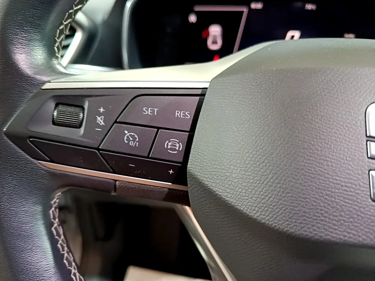 Gros plan sur les commandes à gauche du volant cuir noir du SEAT LEON gris clair 2023, boutons de régulateur de vitesse et assistance conduite.