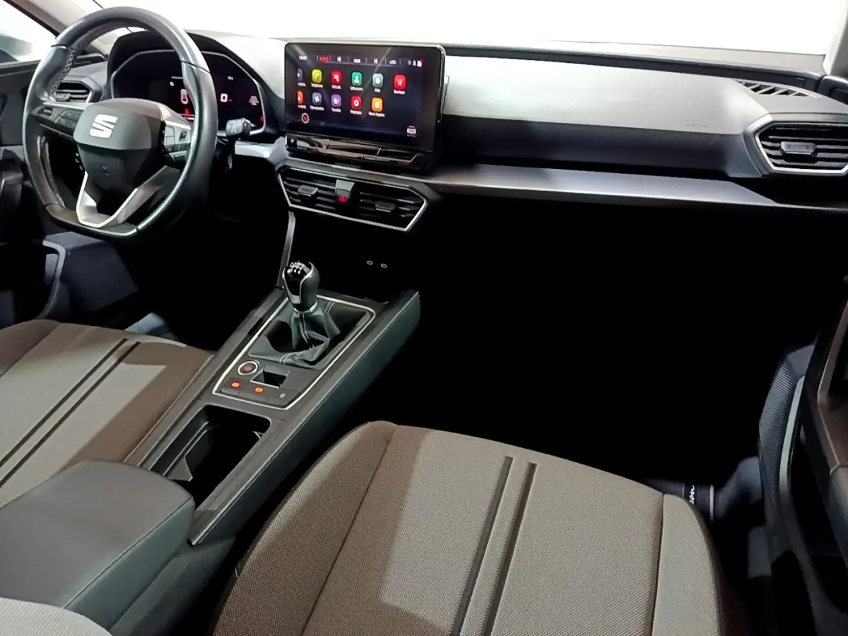 Intérieur avant de la SEAT LEON 2023, vue côté passager, tableau de bord noir avec écran tactile et levier de vitesses manuel.