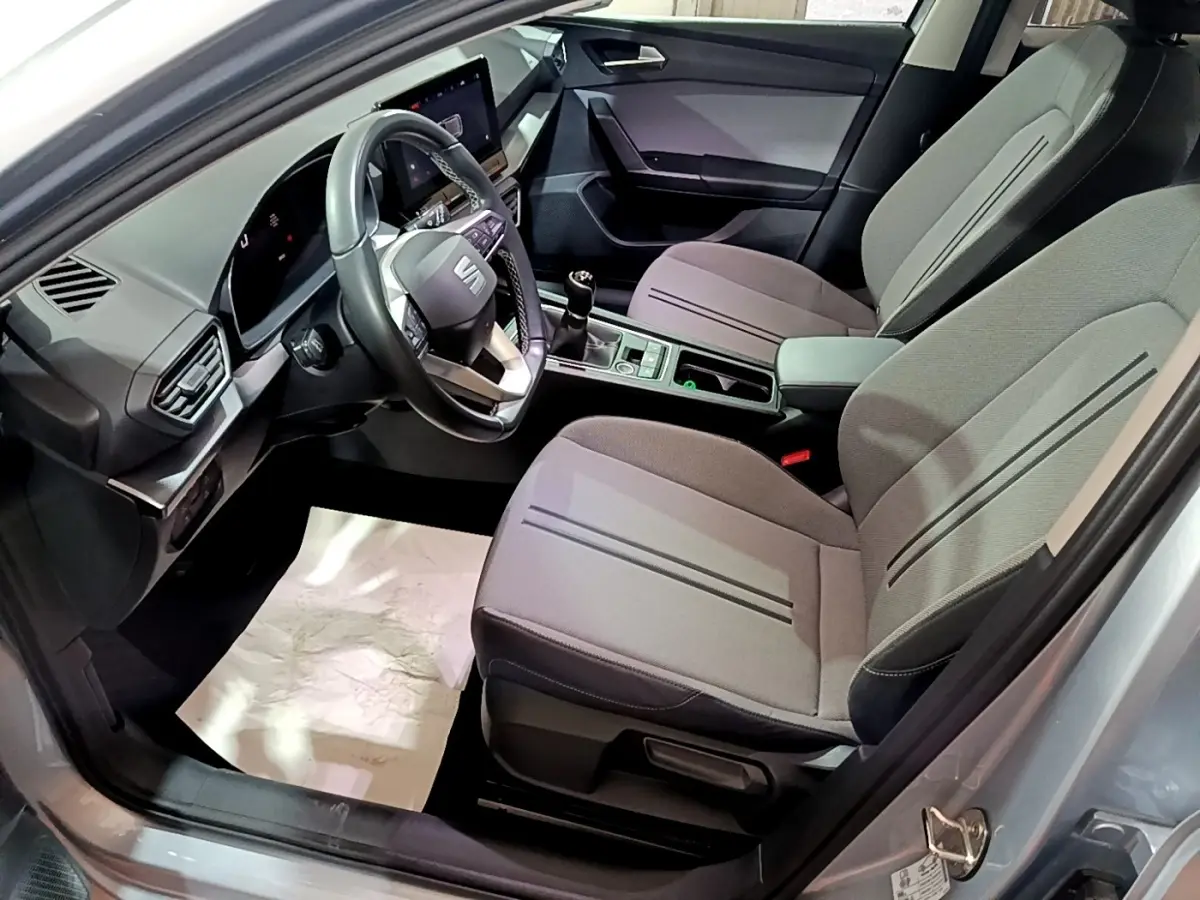 Vue intérieure côté conducteur de la SEAT LEON gris clair 2023, montrant sièges tissu et tableau de bord digital.