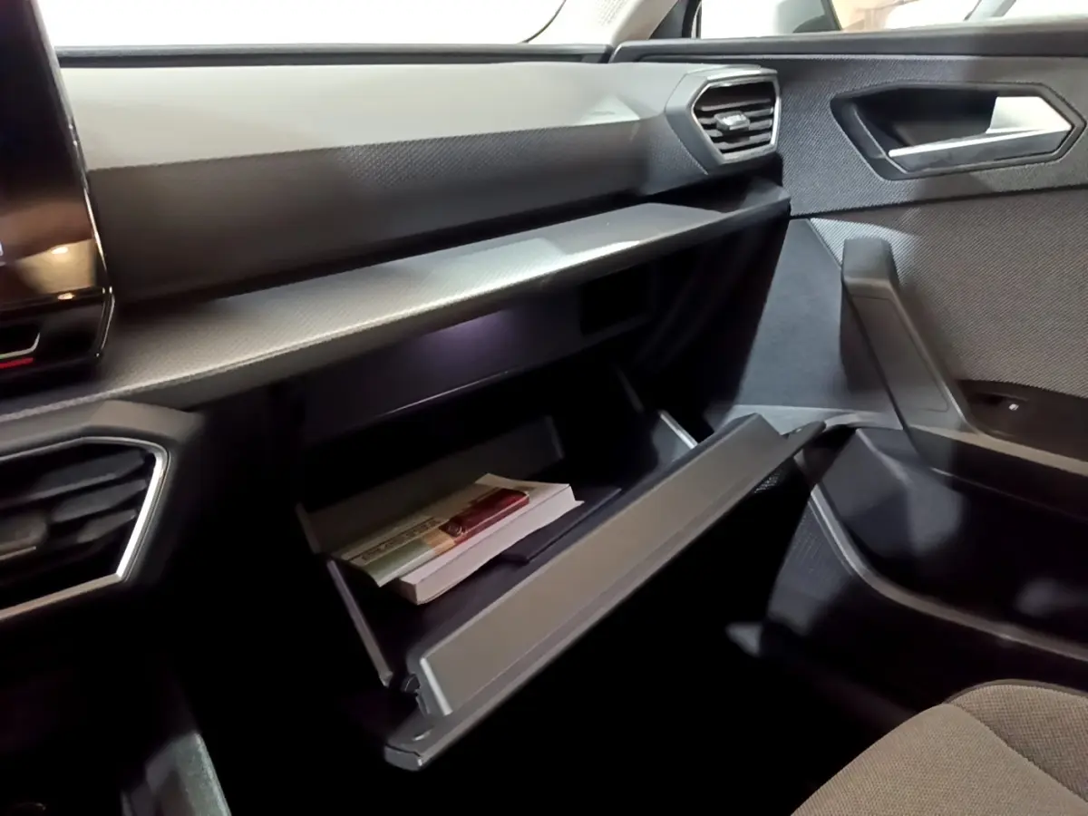Vue intérieure côté passager du SEAT Leon 2023, boîte à gants ouverte avec documents, ambiance sombre et moderne.