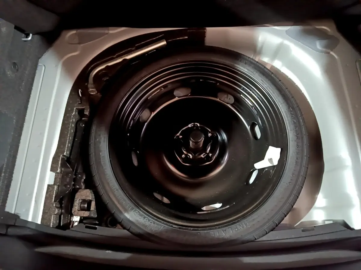 Roue de secours galette noire dans le coffre d'une SEAT Leon 2023, vue plongeante sur le pneu et son emplacement.
