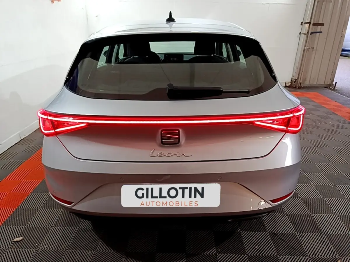 Vue arrière d'une SEAT Leon gris clair 2023 avec feux arrière LED allumés et plaque GILLOTIN Automobiles.
