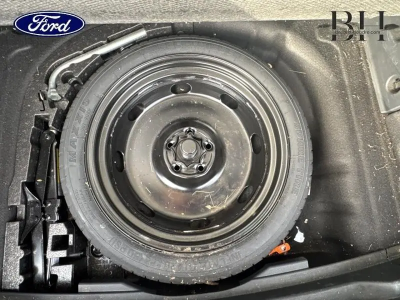 Gros plan sur la roue de secours noire dans le coffre d’un véhicule, entourée d’outils de changement de pneu.