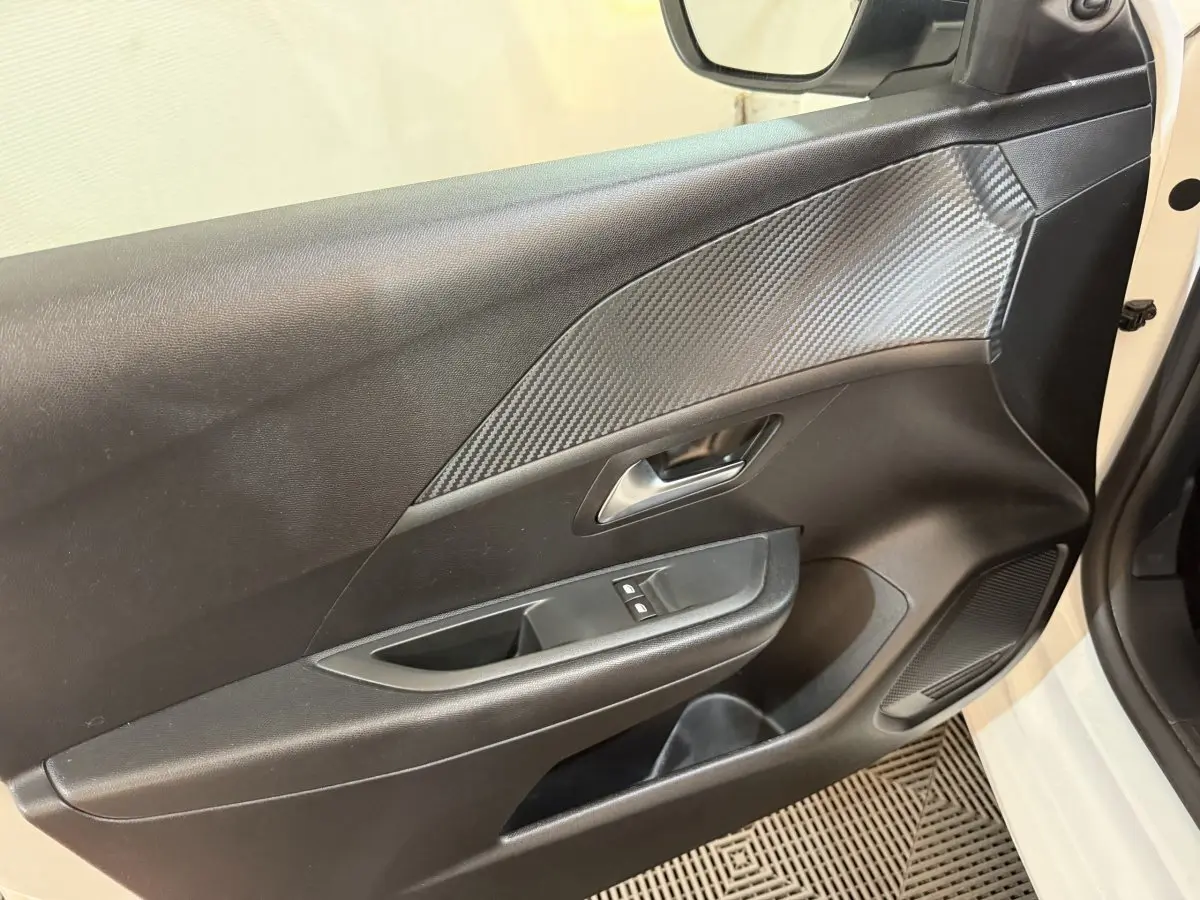 Vue rapprochée de la porte avant gauche noire avec insert effet carbone et commandes de lève-vitres d'une Peugeot 208 2020.