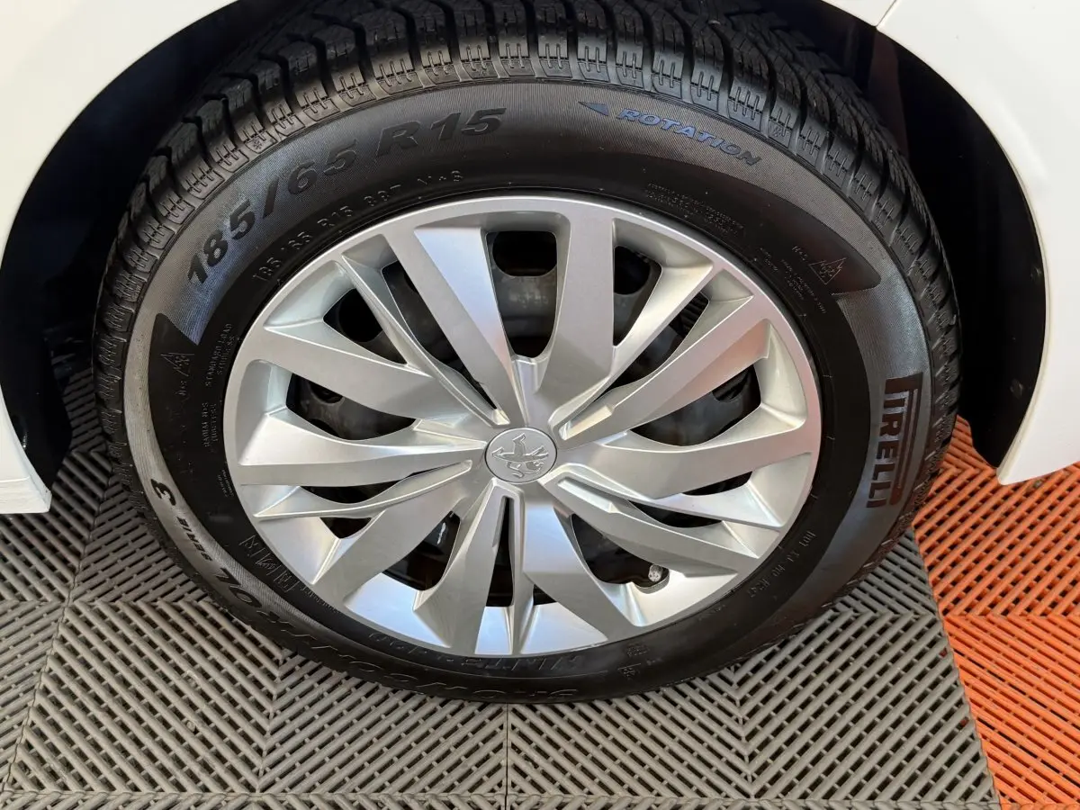 Gros plan sur la roue avant droite d'une Peugeot 208 blanche, mettant en valeur la jante argentée et le pneu Pirelli.