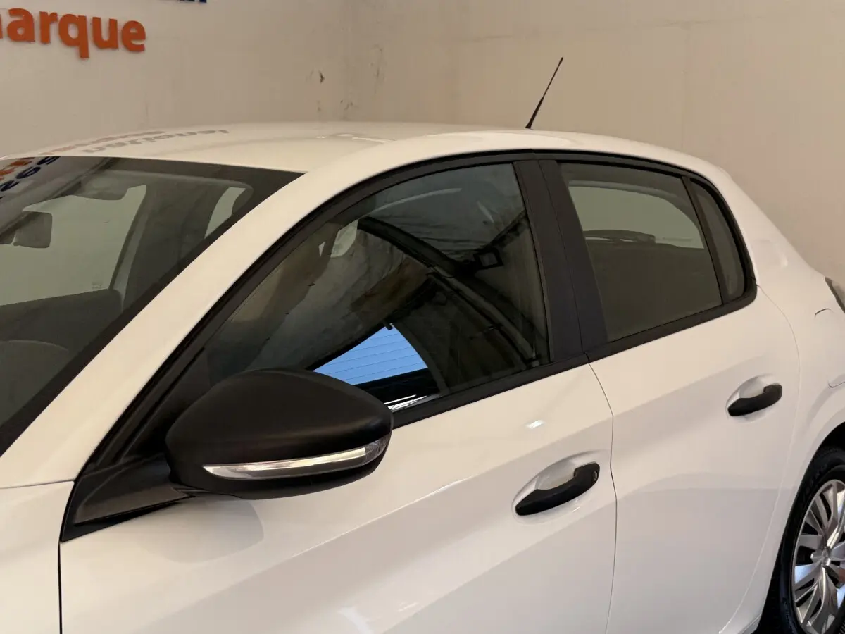 Vue latérale gauche d'une Peugeot 208 blanche avec rétroviseur noir et poignées de porte noires.