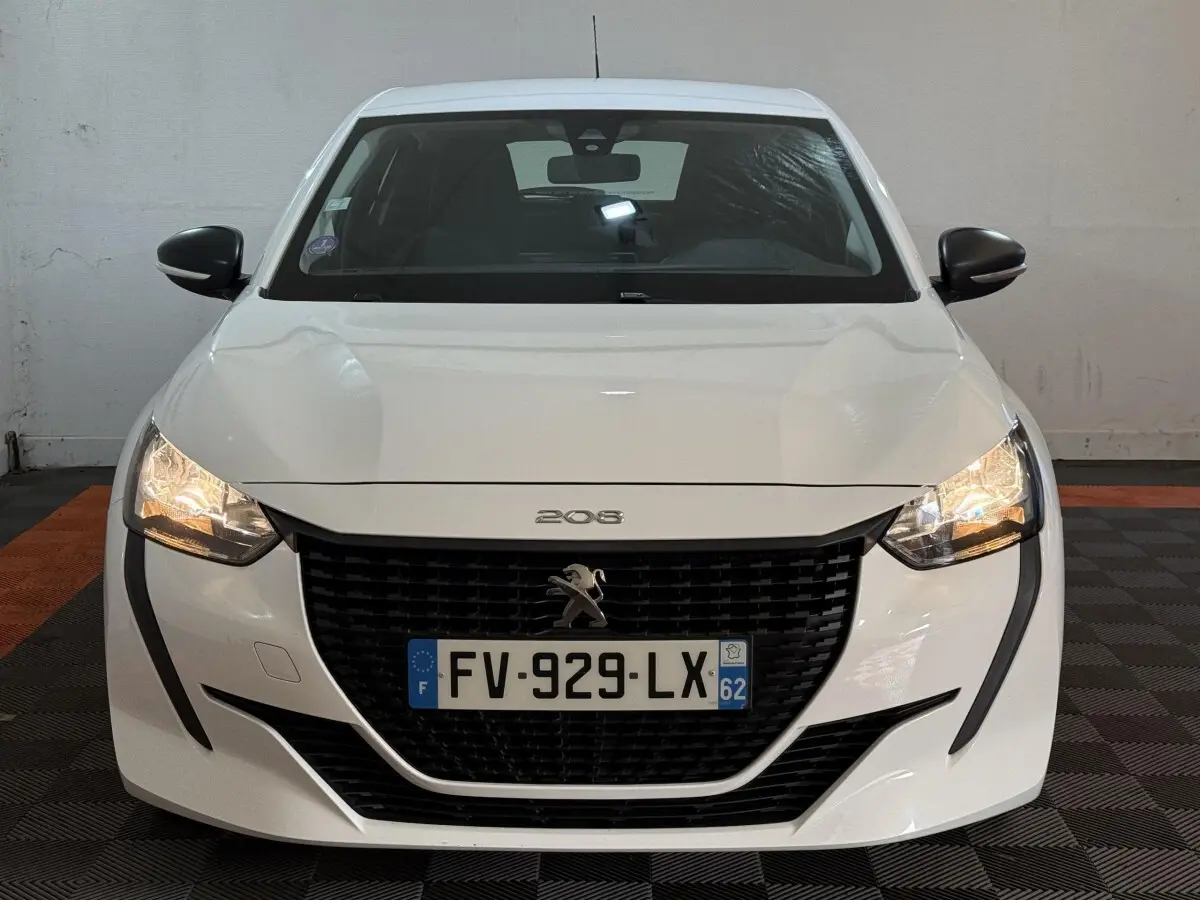 Vue frontale d'une Peugeot 208 blanche avec phares allumés et calandre noire distinctive.