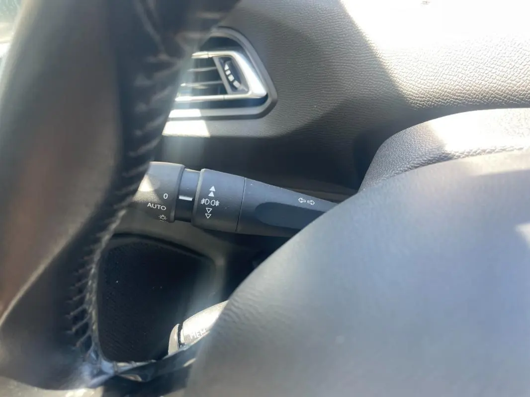 Détail du commodo d’éclairage côté gauche du volant dans l’habitacle d’une Peugeot 308 blanche de 2020.