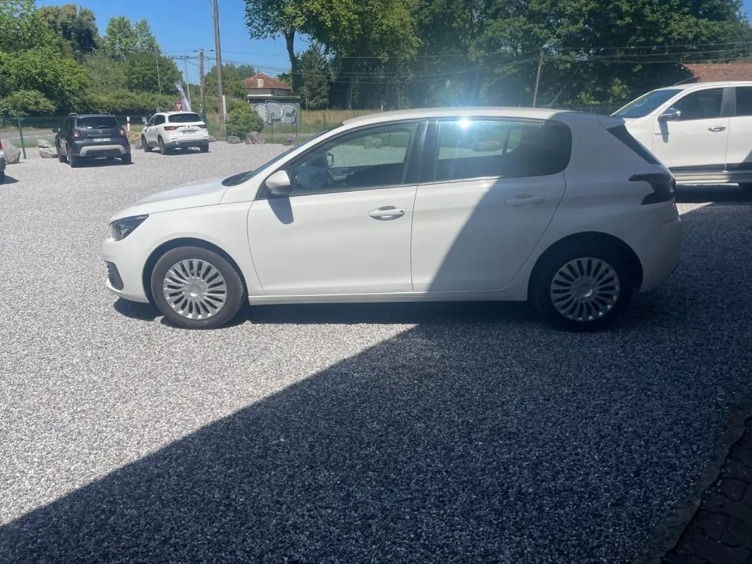 Peugeot 308 blanc vue de profil côté gauche sur un parking extérieur, avec jantes à rayons fins.