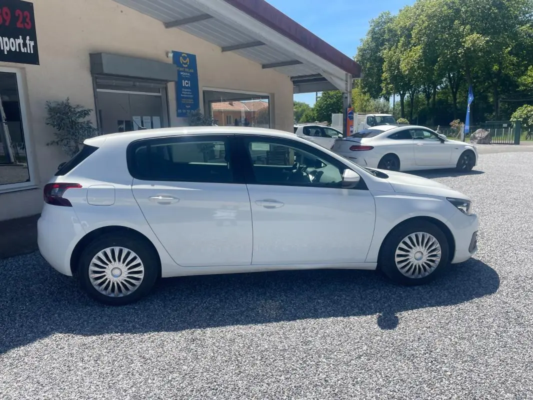 Peugeot 308 blanc vue de profil côté gauche, avec jantes à enjoliveurs et carrosserie 5 portes sous un ciel dégagé.