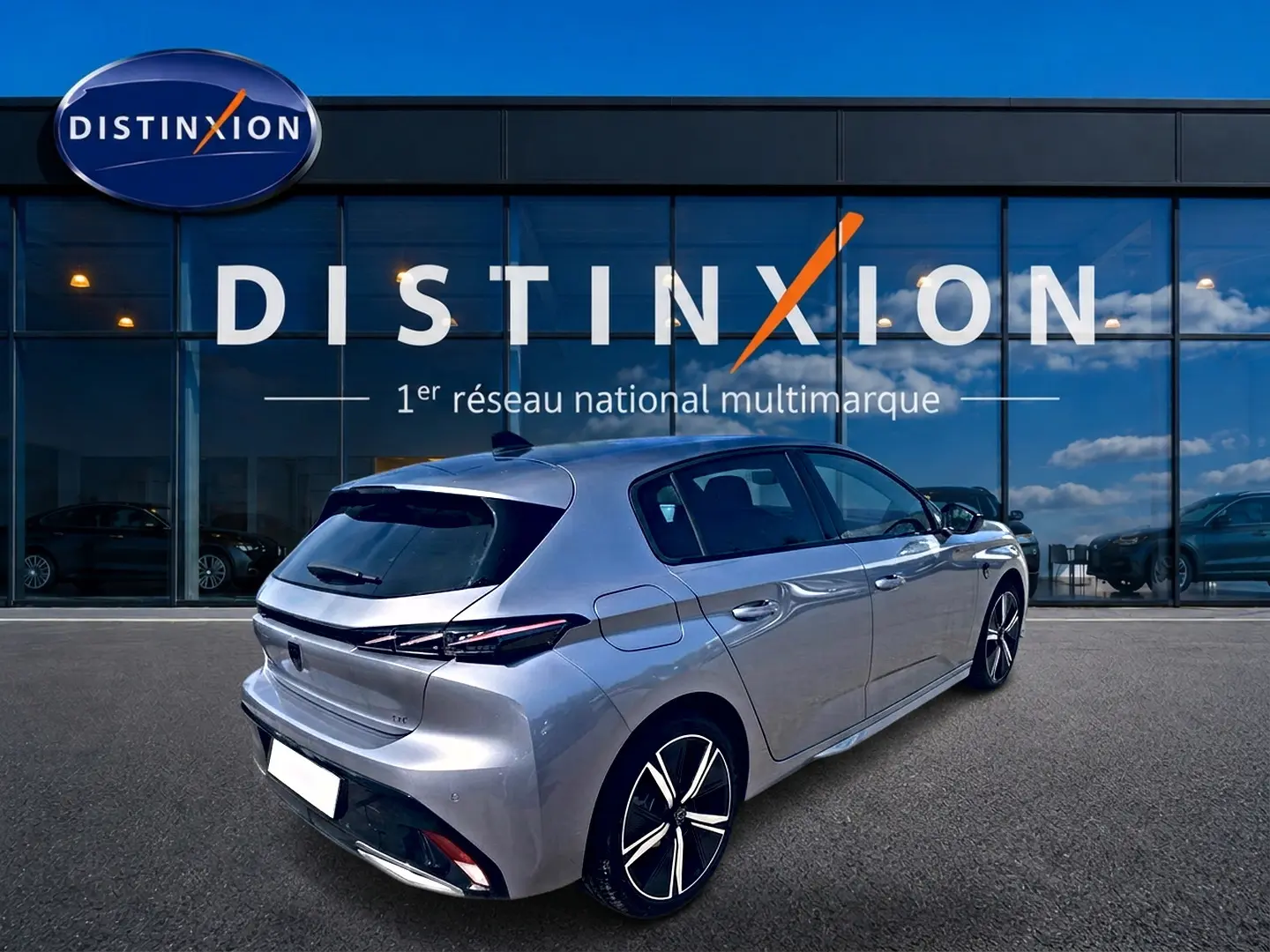 Peugeot 308 gris vue 3/4 arrière droit, avec jantes alu et feux arrière à LED, devant un showroom Distinxion.