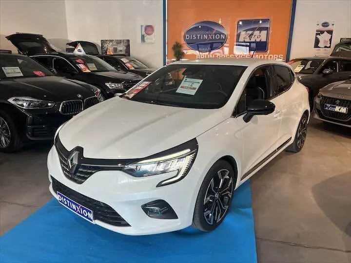 Renault Clio V blanc nacré vue 3/4 avant droit en showroom avec jantes noires et toit noir.