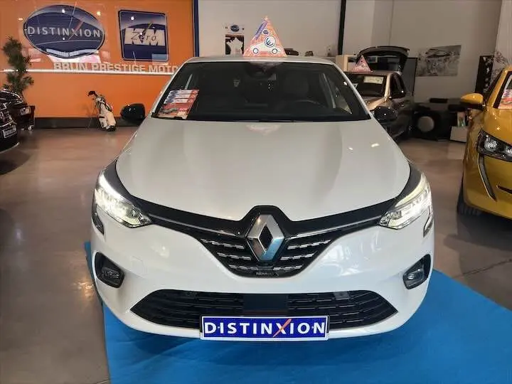 Vue frontale d'une Renault Clio V blanche nacrée en showroom avec plaque Distinxion visible.