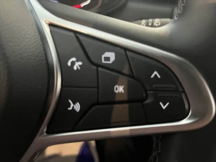 Gros plan sur les commandes noires du volant de la Renault Clio V blanc nacré, avec boutons de navigation et téléphone.