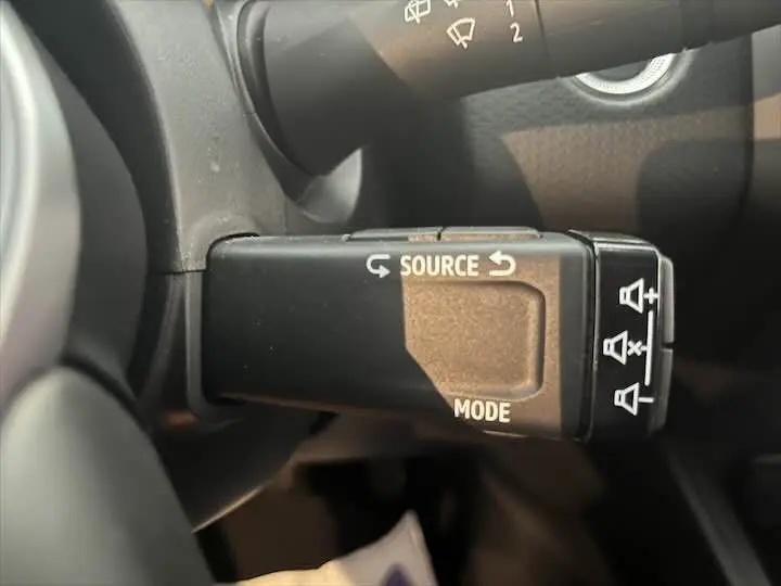 Commande au volant noire avec boutons source et mode sur Renault Clio V blanc nacré, vue de près côté gauche.