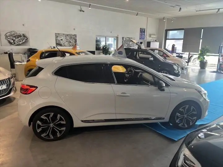 Vue latérale côté gauche d'une Renault Clio V blanche nacrée en showroom avec jantes noires et détails chromés.