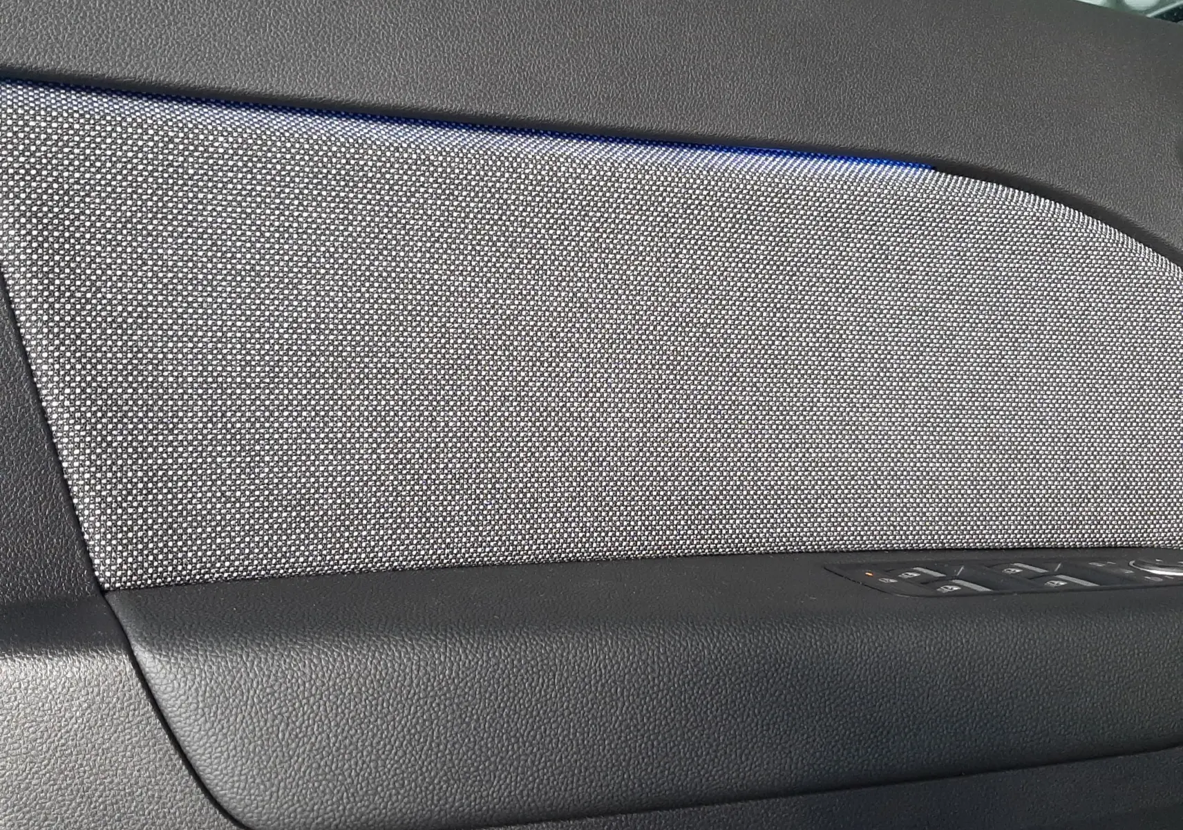 Détail de la garniture intérieure côté gauche de porte du Renault Captur E-Tech Hybrid 2024 avec tissu gris et éclairage bleu.