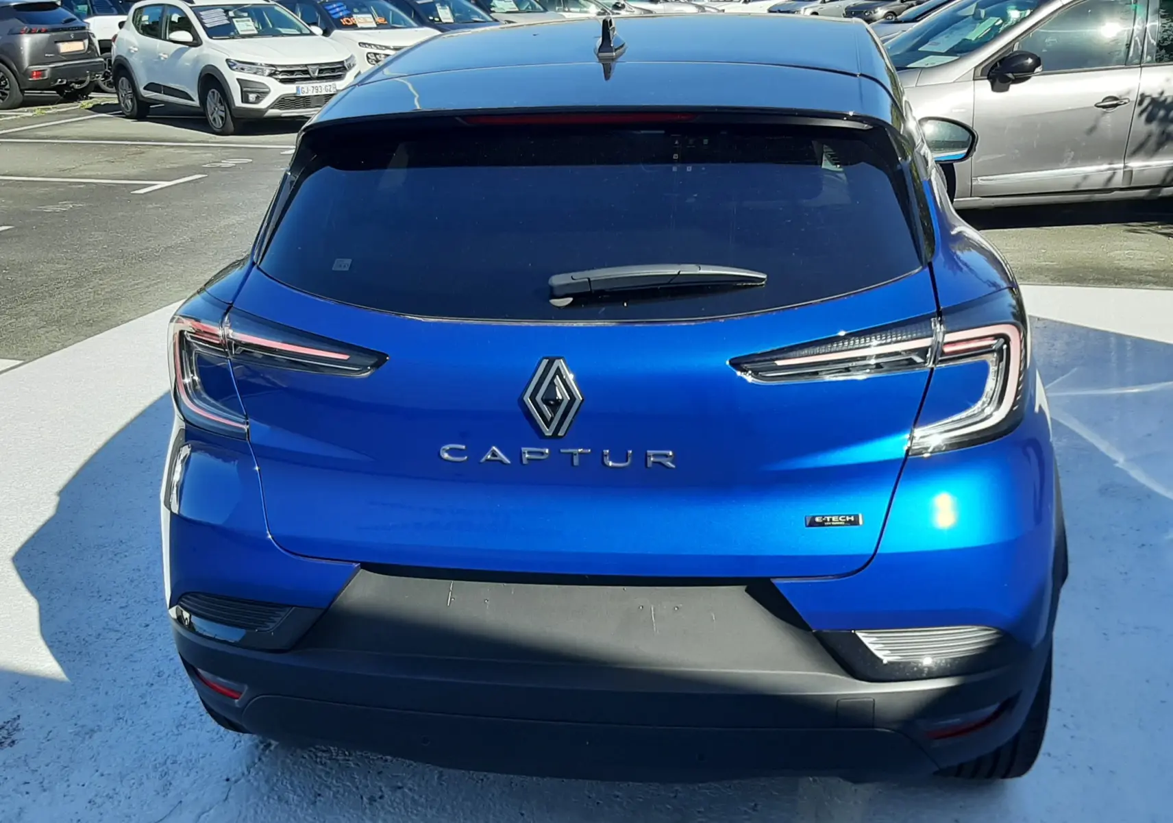 Vue arrière d'un Renault Captur E-Tech Hybrid 145ch en bleu Iron avec toit noir, mettant en valeur ses feux LED distinctifs.