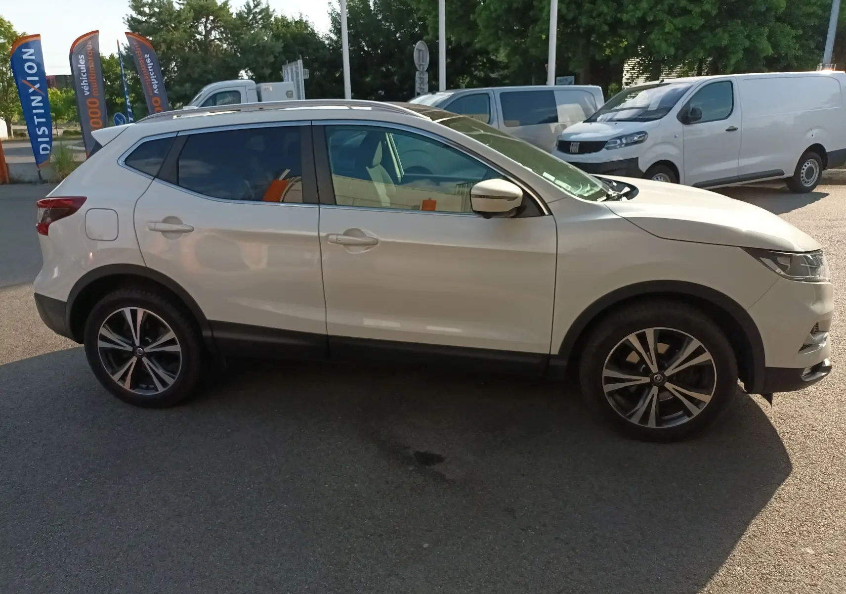 Profil côté gauche d'un Nissan Qashqai blanc nacré 2019 avec jantes alliage bicolores et vitres teintées.