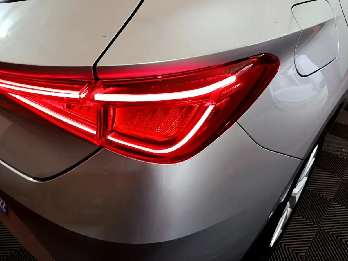 Gros plan sur le feu arrière droit rouge allumé d'une SEAT LEON gris foncé, avec la trappe à carburant visible.
