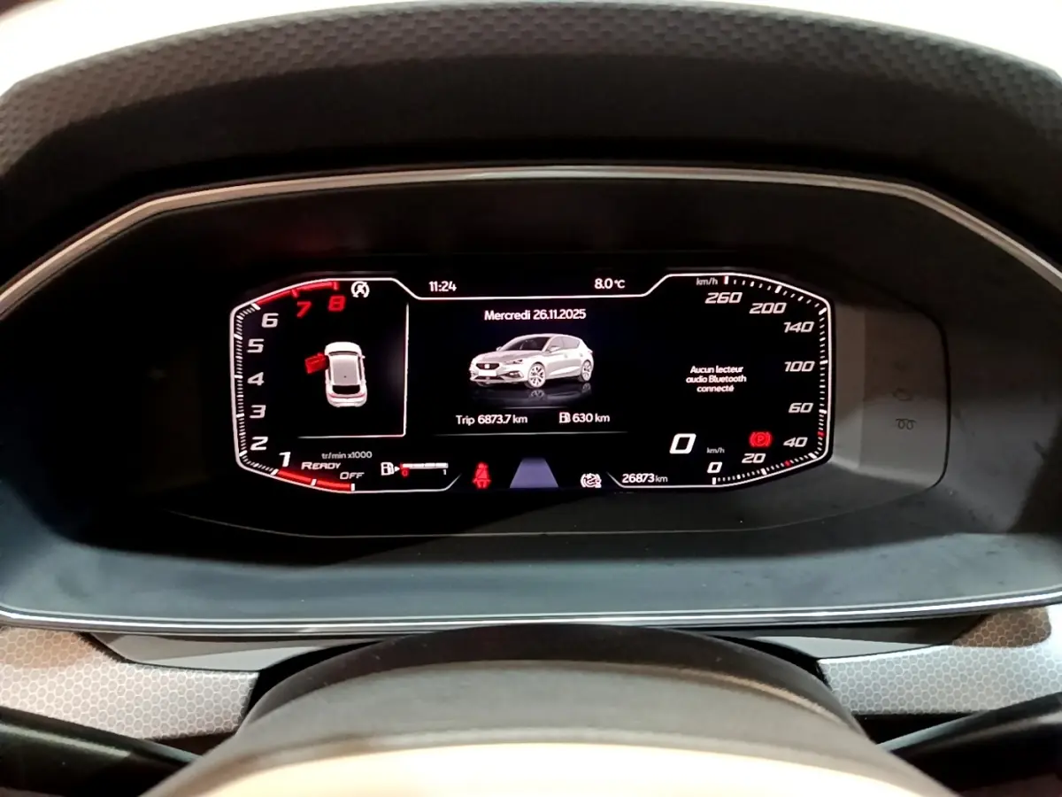 Vue rapprochée du tableau de bord numérique de la SEAT LEON 2023 affichant vitesse, compte-tours et image du véhicule gris foncé.