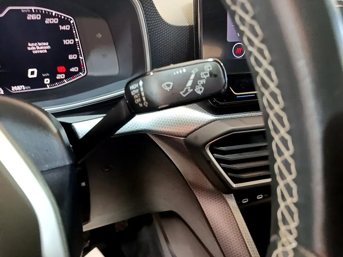 Gros plan sur le tableau de bord et le commodo d’essuie-glace d’une SEAT Leon gris foncé, affichage digital visible.